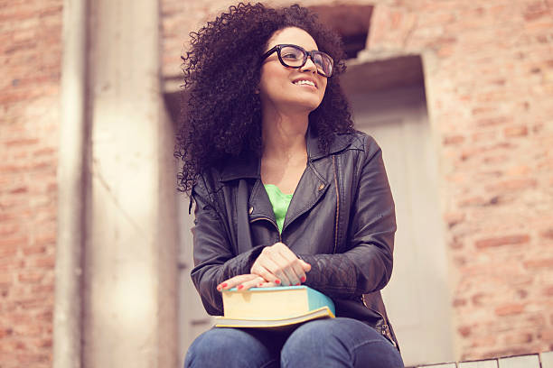 African american young woman smiling with books and glasses outdoors